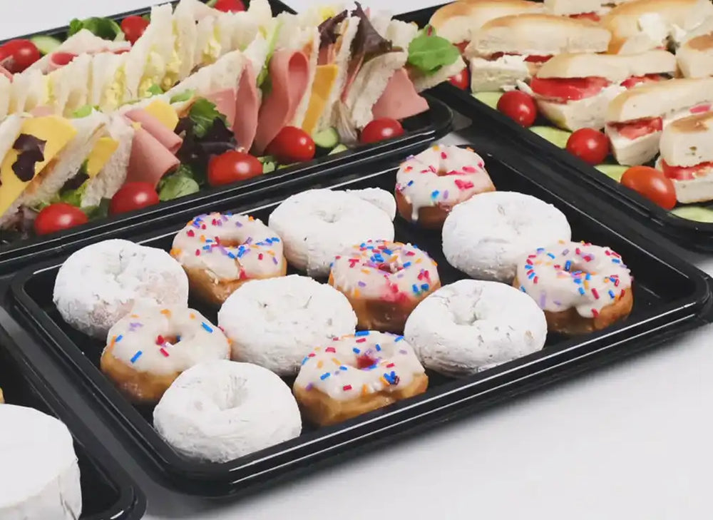 Black platter containing powdered and frosted donuts decorated with red and blue sprinkles.