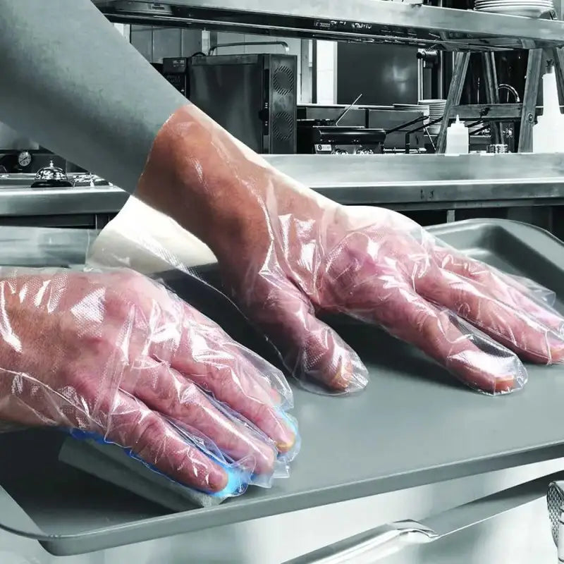 Hands in disposable plastic gloves in a kitchen using Clear Embossed Polythene Gloves