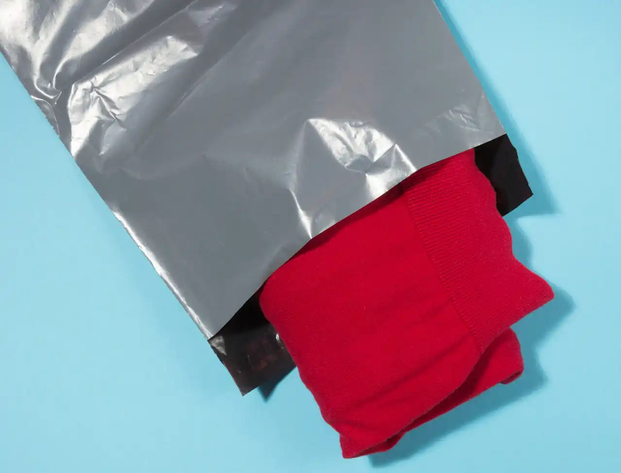 Red fabric or clothing emerging from a silver plastic shipping bag.