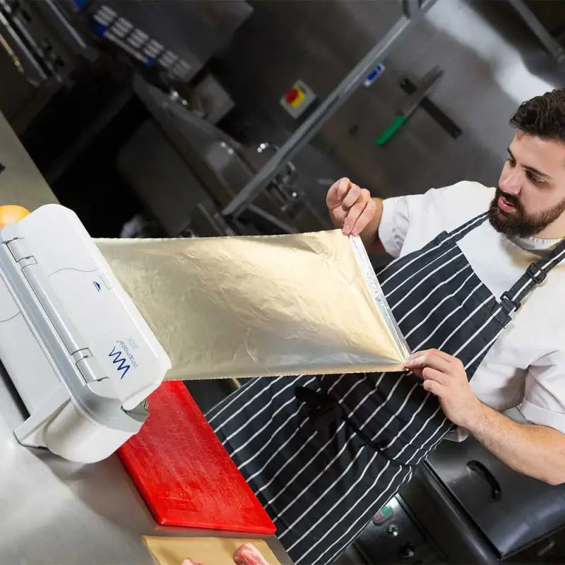 Chef in a striped apron rolls pasta dough through a machine with Aluminium Foil 24C54 nearby